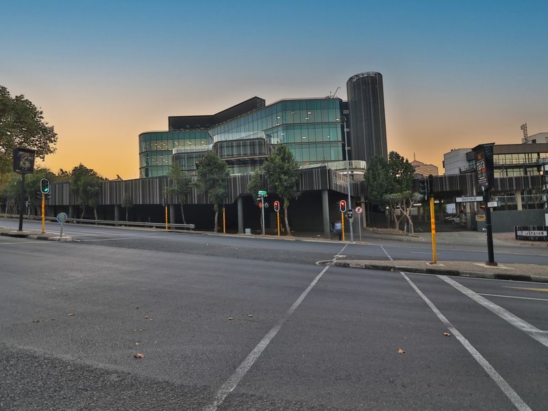 A modern multi-story commercial office building featuring a glass facade and integrated covered parking, situated at a prominent street intersection.