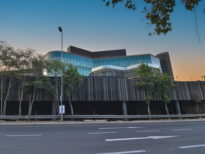 Modern commercial building facade featuring a glass curtain wall, contemporary vertical slat cladding, and structural support columns, viewed from the street.