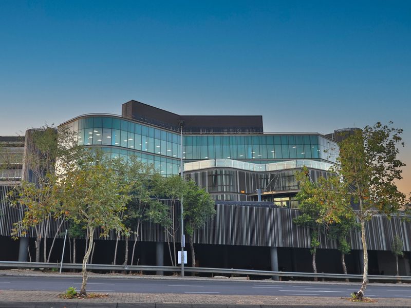 Modern commercial office building featuring a striking glass curtain wall, architectural louvred screening, and a prominent ground-level reception entrance.