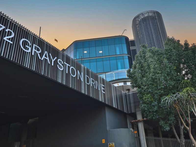 Modern commercial building facade featuring a glass curtain wall, vertical louvre detailing, and prominent street address signage.