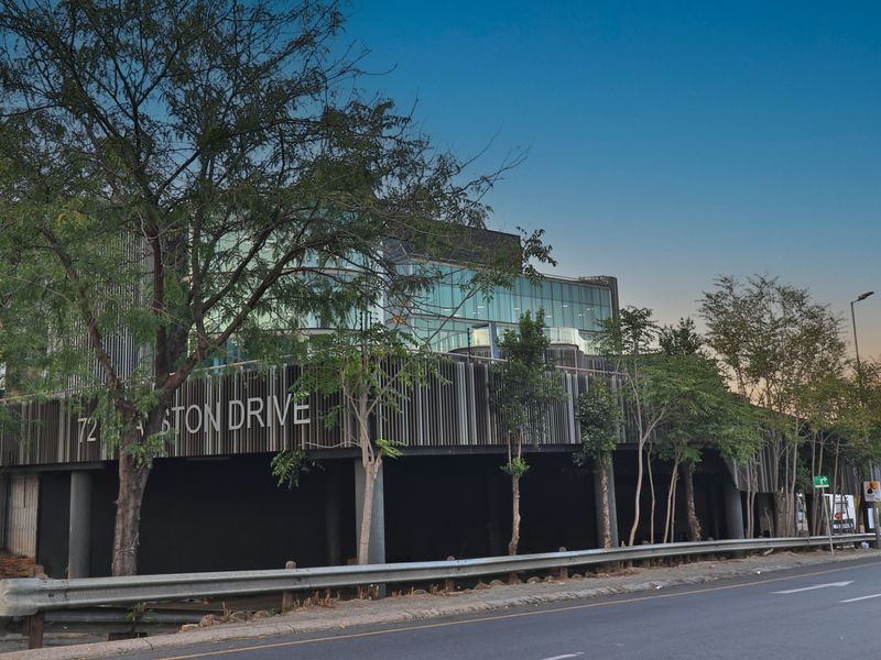 Modern commercial building facade featuring a glass curtain wall, vertical slat cladding, and prominent street-level signage on a landscaped site.
