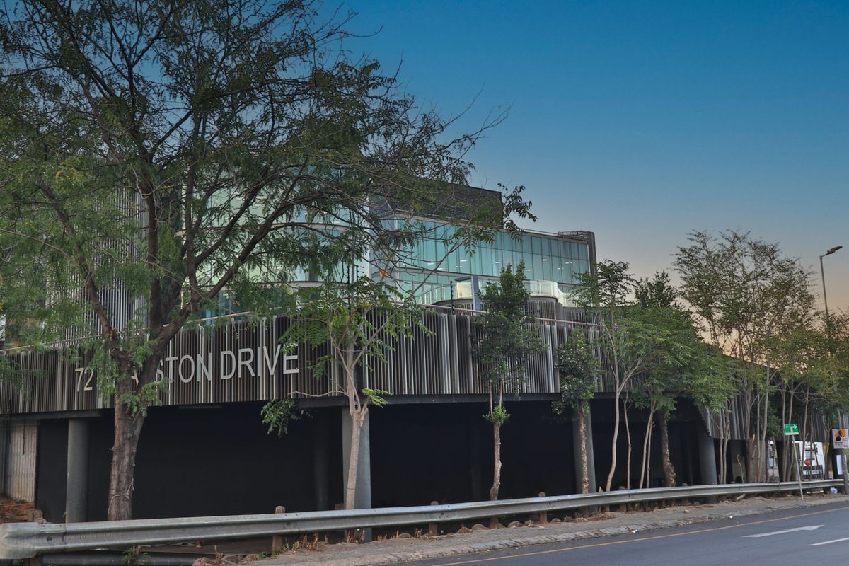 Modern commercial building facade featuring a glass curtain wall, vertical slat cladding, and prominent street-level signage on a landscaped site.