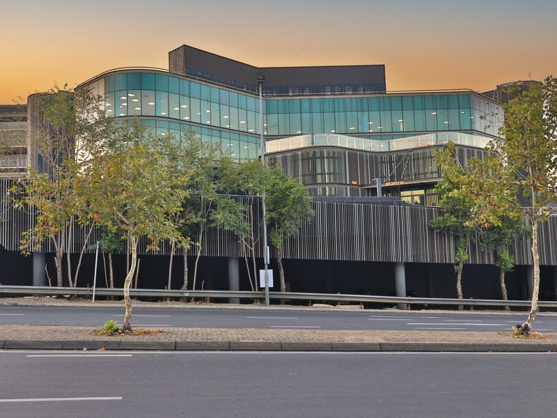 Modern commercial office building featuring a striking glass facade, architectural louvred screening, and a prominent reception entrance at street level.
