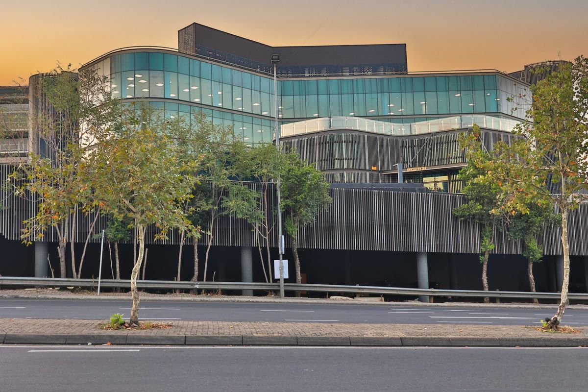 Modern commercial office building featuring a striking glass facade, architectural louvred screening, and a prominent reception entrance at street level.