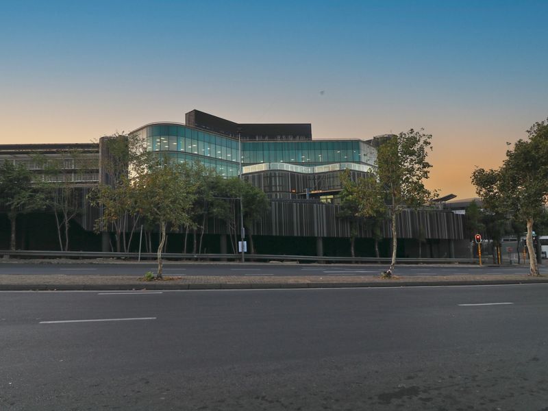 Street-level view of a modern commercial building featuring a glass facade, vertical timber cladding, and integrated multi-level parking structure.
