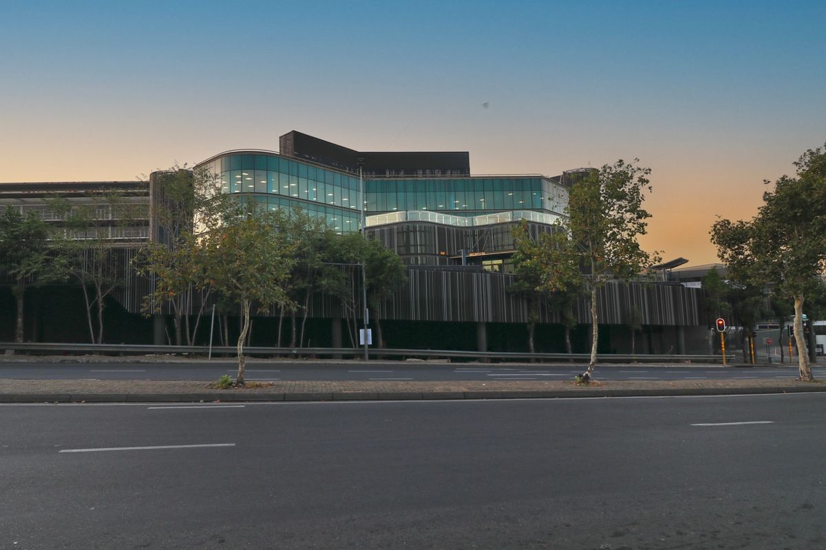 Street-level view of a modern commercial building featuring a glass facade, vertical timber cladding, and integrated multi-level parking structure.