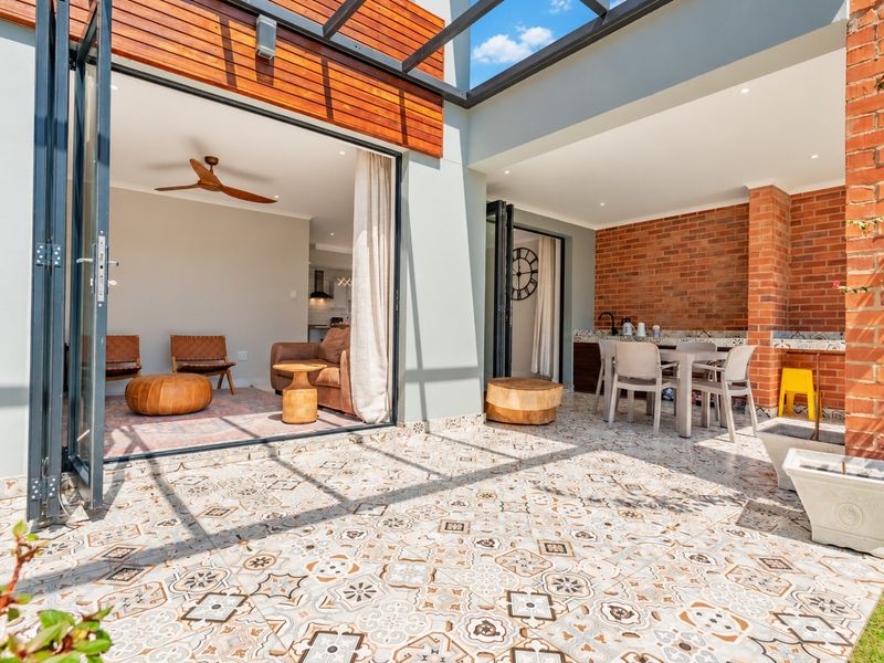 A modern covered patio featuring patterned floor tiles, exposed brick accents, and bi-fold doors that seamlessly connect the outdoor space to the interior living area.