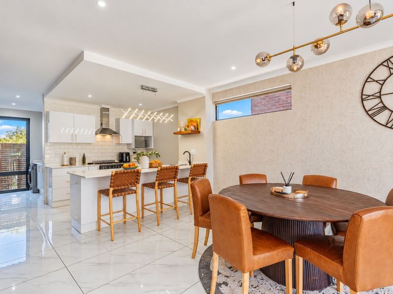 Modern open-plan kitchen and dining area featuring a central island, stone benchtops, subway tile splashback, and high-gloss porcelain flooring throughout.
