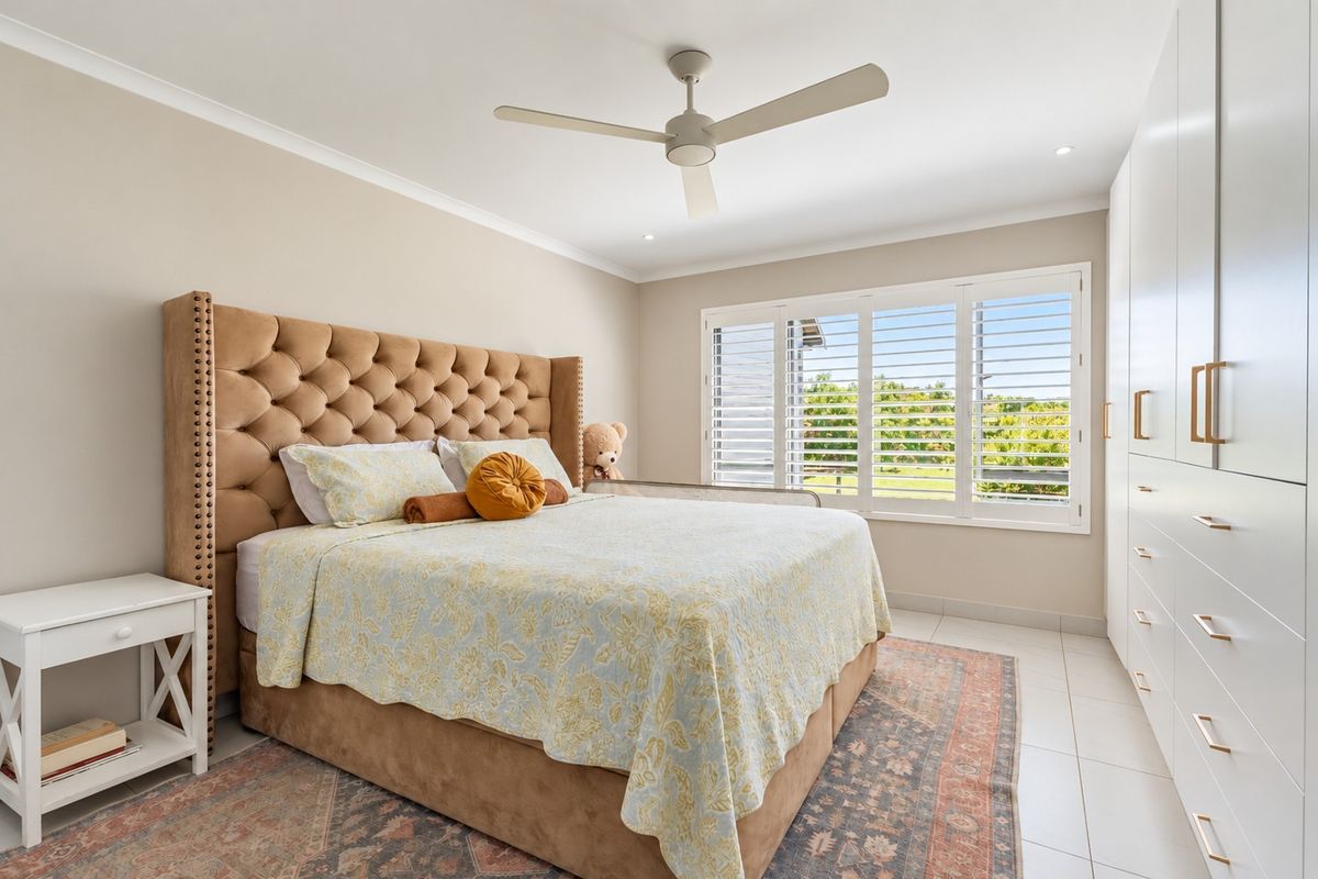 A well-maintained bedroom featuring tiled flooring, built-in wardrobes, plantation shutters, and a ceiling fan, offering a bright and comfortable living space.
