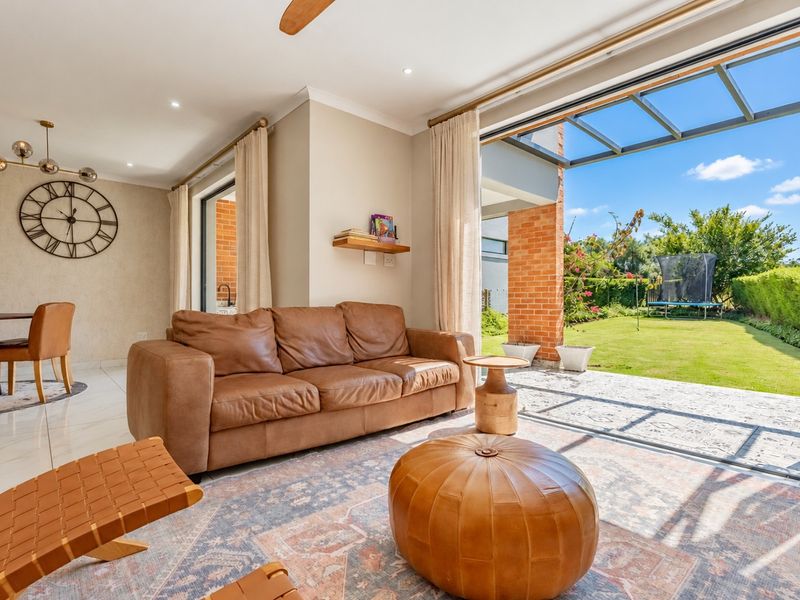Bright open-plan living area featuring tiled floors, recessed lighting, and seamless flow through large stacking doors to a covered patio and garden.