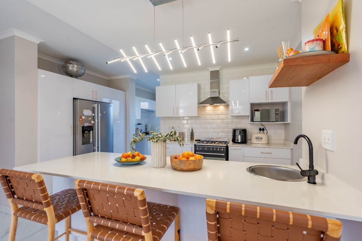 Modern kitchen featuring white gloss cabinetry, subway tile backsplash, stone countertops, integrated appliances, and a central island with a secondary sink.