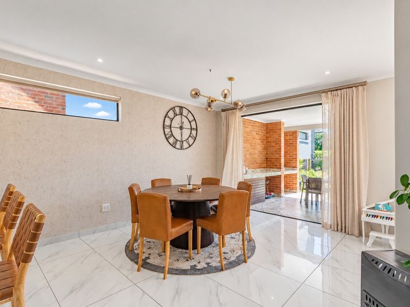 Bright open-plan dining area featuring polished marble-look tiles, recessed lighting, and seamless flow to a covered brick-built outdoor patio and braai area.