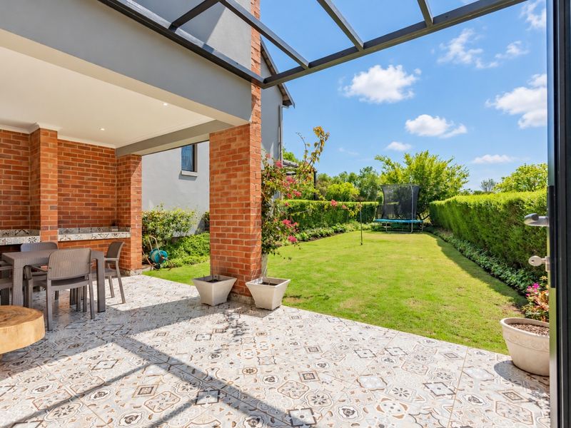 Covered patio featuring a built-in braai, decorative tiled flooring, and brick pillars, overlooking a well-maintained private garden.