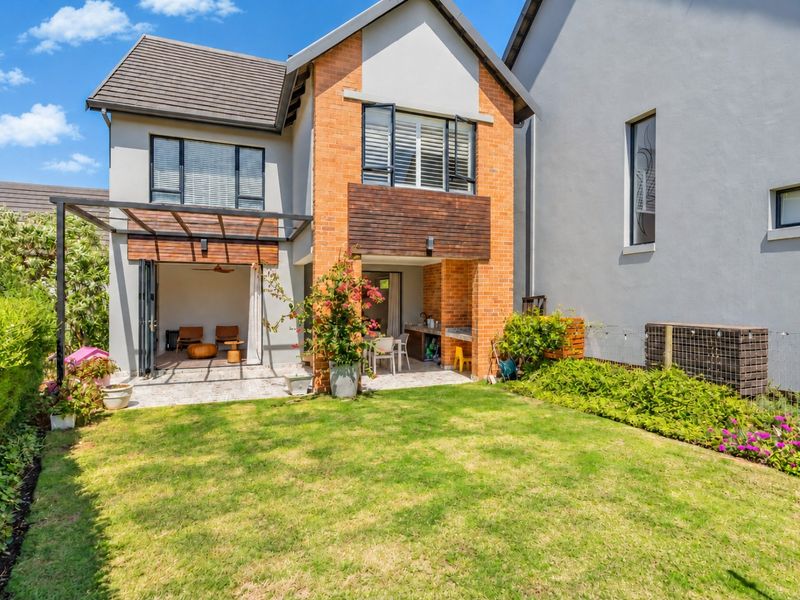 Rear view of a townhouse featuring a landscaped garden, a covered patio with a built-in braai, and modern bi-fold doors leading to the interior.