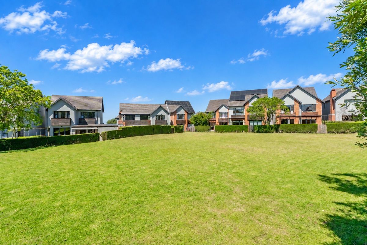 A wide-angle view of the rear of the townhouse complex, featuring well-maintained lawns, manicured hedging, and multiple residential units with solar panel installations.