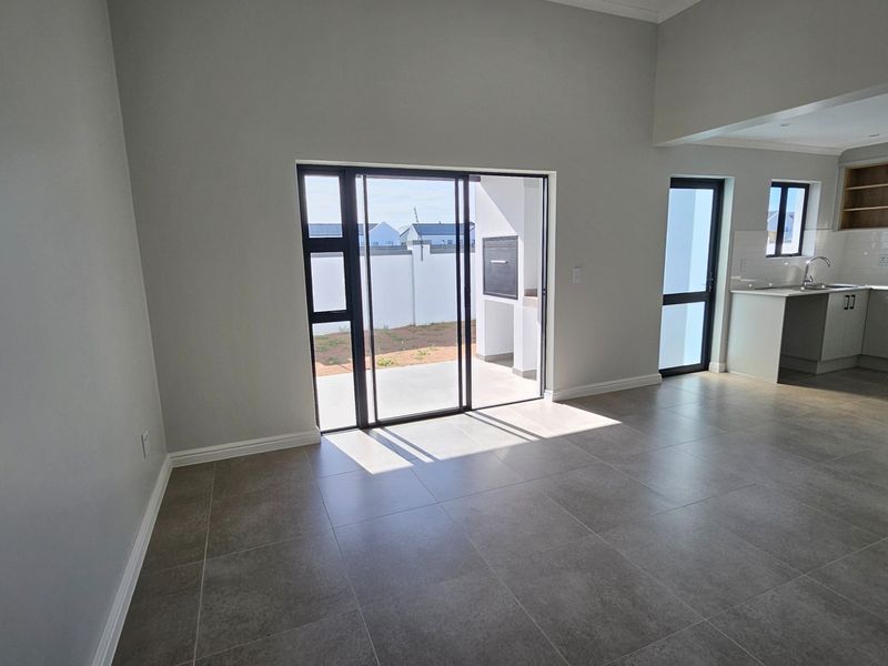 Spacious open-plan living area featuring modern tiled floors, neutral walls, and a sleek kitchen with built-in appliances, leading out to a patio.