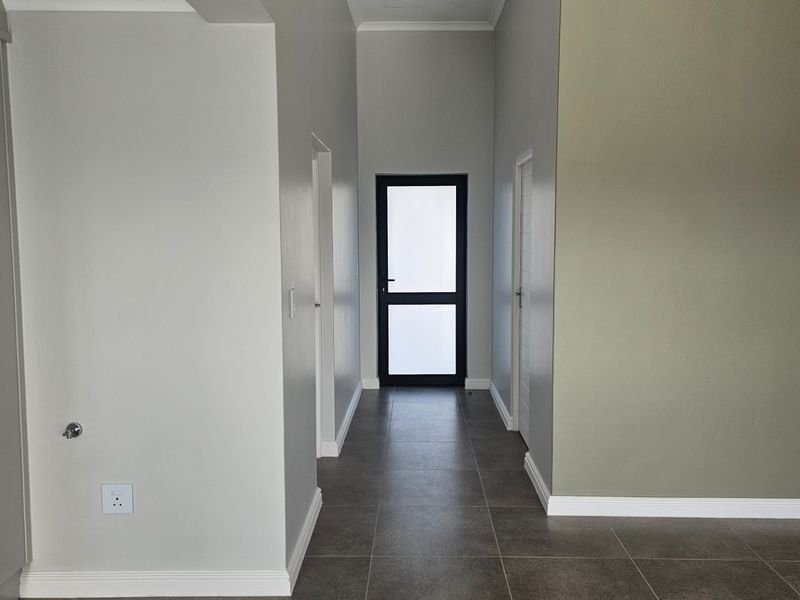 A clean, modern hallway featuring neutral wall tones, tiled flooring, and access to multiple rooms through internal doors.