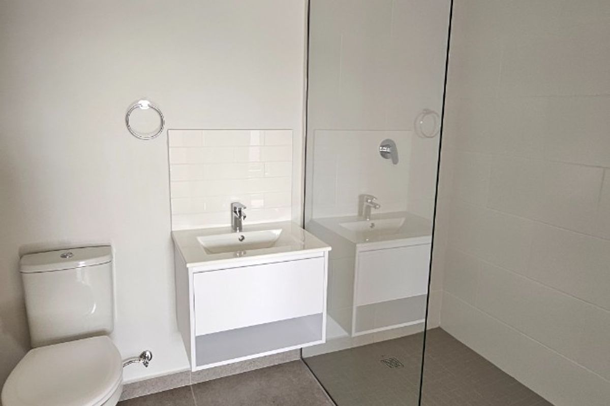Modern bathroom featuring a wall-mounted vanity, toilet, and a spacious walk-in shower with a frameless glass screen and neutral floor tiling.