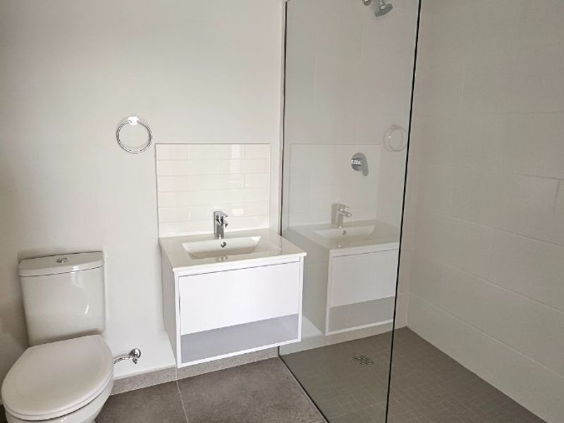 Modern bathroom featuring a wall-mounted vanity, toilet, and a spacious walk-in shower with a frameless glass screen and neutral floor tiling.