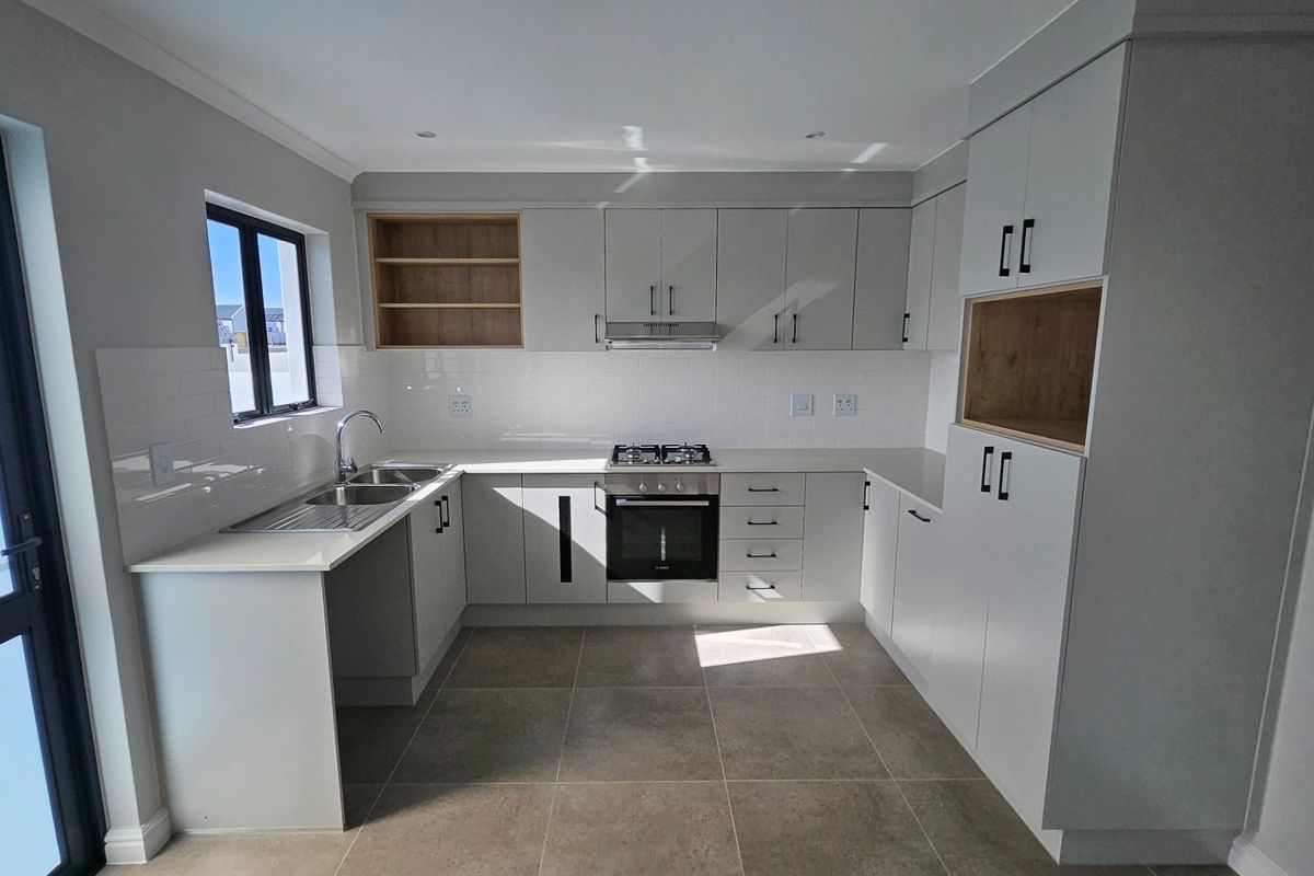 Modern kitchen featuring sleek cabinetry, stone countertops, integrated gas hob, oven, extractor fan, and subway tile backsplash with neutral tiled flooring.