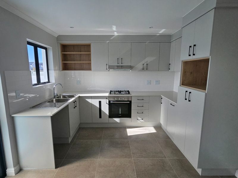 Modern kitchen featuring sleek cabinetry, stone countertops, integrated gas hob, oven, extractor fan, and subway tile backsplash with neutral tiled flooring.