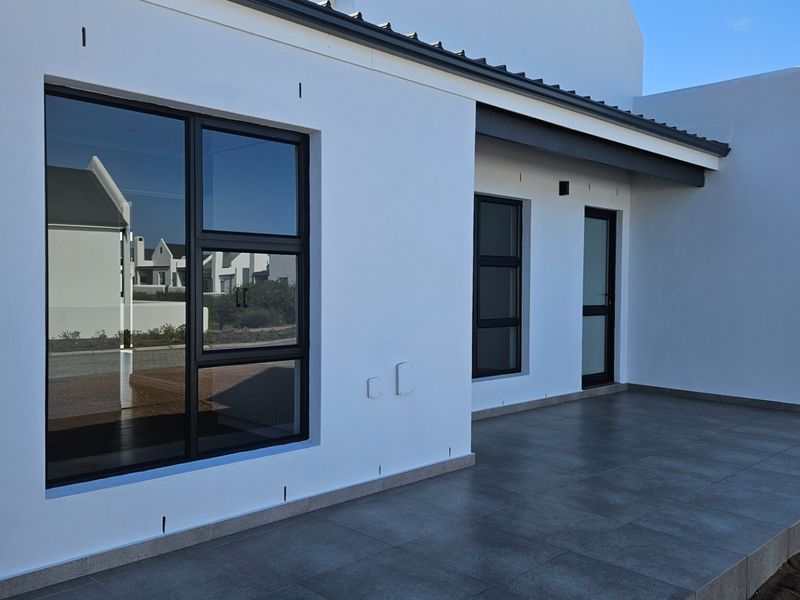 A modern, covered patio area featuring sleek tiled flooring and dark aluminium window and door frames, offering a clean and contemporary outdoor living space.
