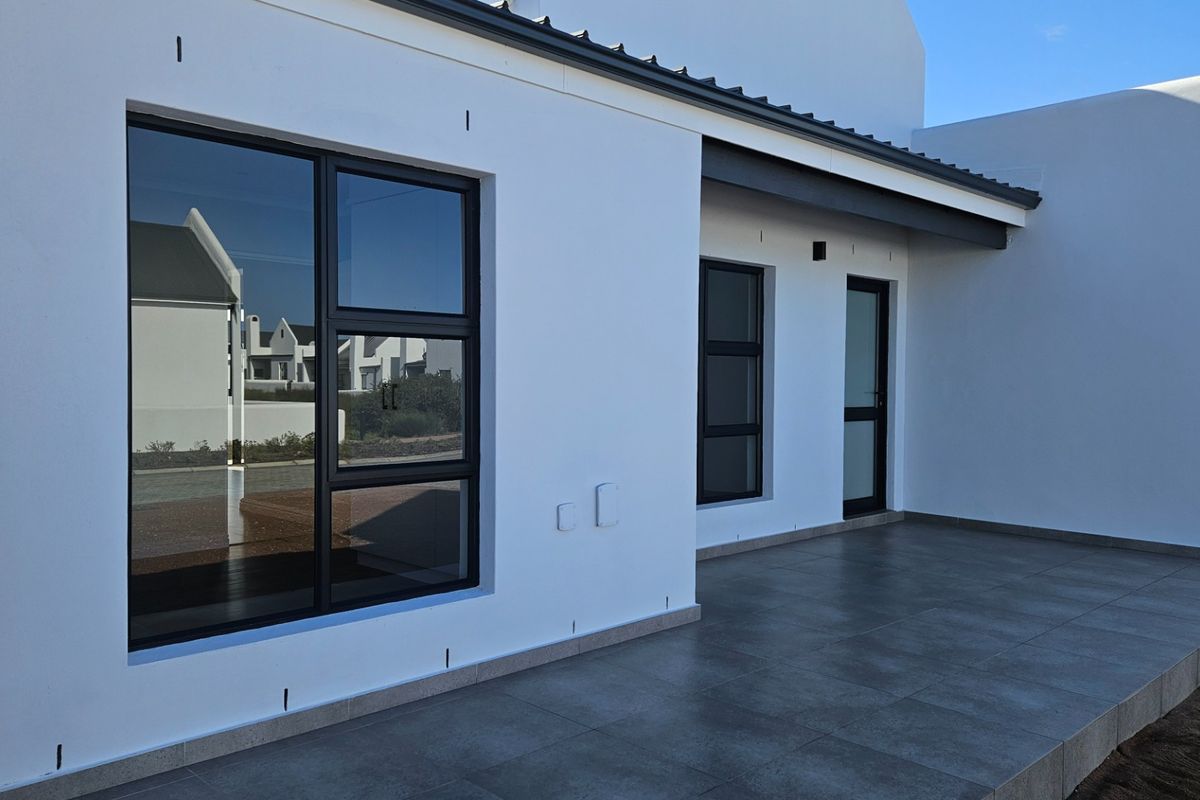 A modern, covered patio area featuring sleek tiled flooring and dark aluminium window and door frames, offering a clean and contemporary outdoor living space.