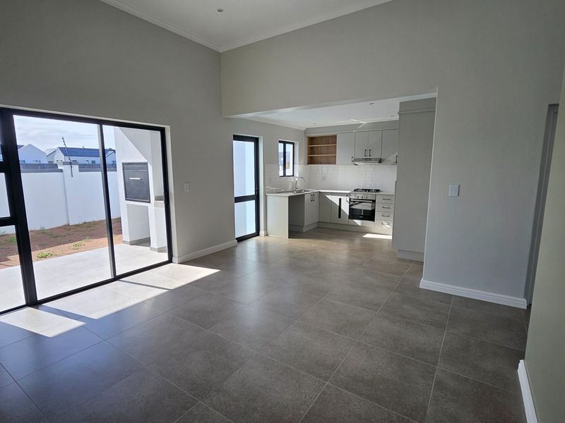 Spacious open-plan living area featuring modern tiled floors, a sleek kitchen with built-in appliances, and large sliding doors leading to an outdoor patio.