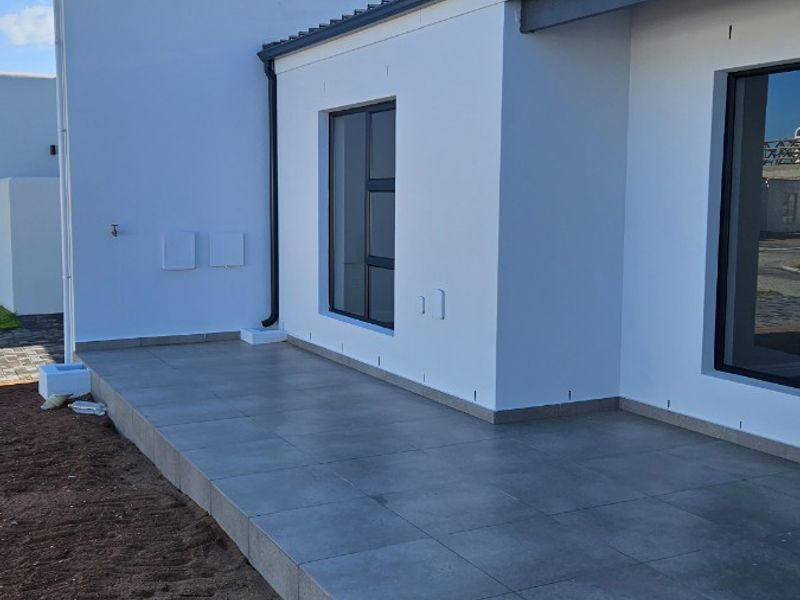A modern, tiled patio area featuring clean white exterior walls and dark aluminium window frames, currently awaiting final landscaping completion.
