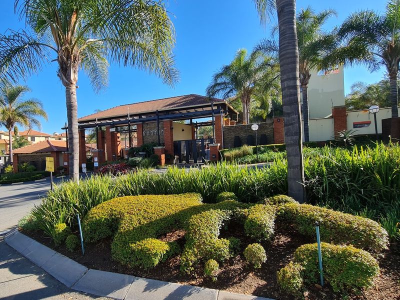 The main entrance to the apartment complex featuring a secure gated access point, brick architectural detailing, and well-maintained landscaped gardens.