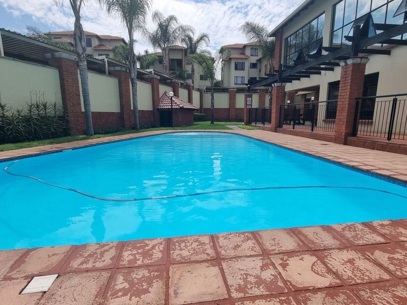 A communal swimming pool area featuring brick paving, perimeter walls, and a pergola structure within an apartment complex setting.