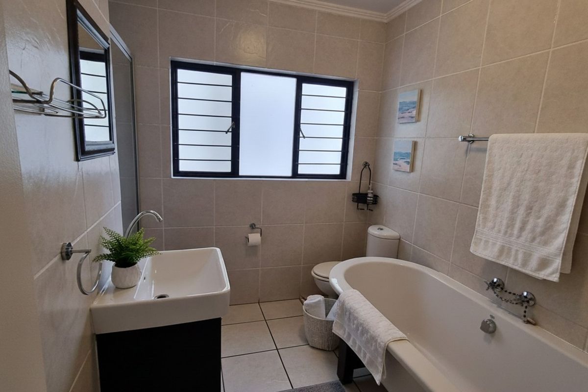 A well-maintained bathroom featuring a bathtub, vanity basin, toilet, and neutral wall and floor tiling with a window for natural light.