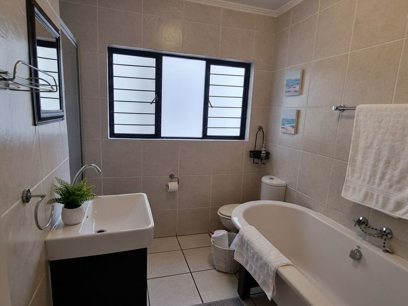 A well-maintained bathroom featuring a bathtub, vanity basin, toilet, and neutral wall and floor tiling with a window for natural light.