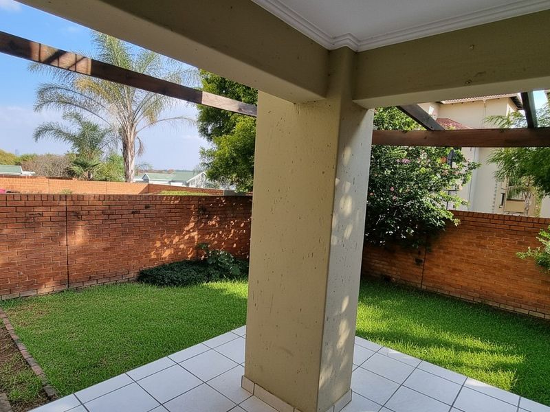 A covered patio area featuring tiled flooring, a concrete support pillar, and a timber pergola, overlooking a private garden with brick boundary walls.