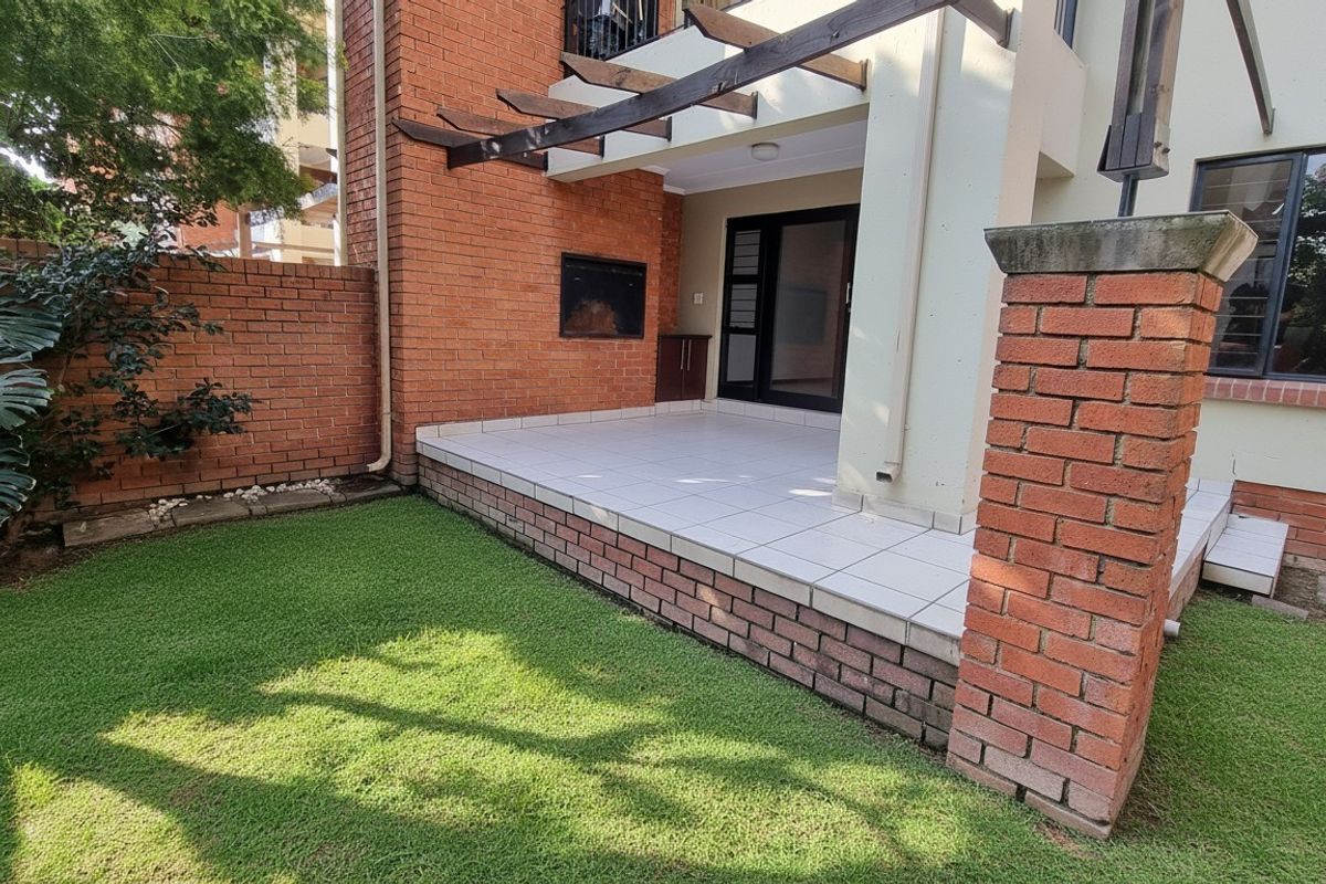 A private patio area featuring a built-in braai, tiled flooring, and a timber pergola, overlooking a small garden space.