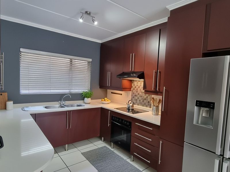 Modern kitchen featuring dark wood cabinetry, stone countertops, integrated appliances, and tiled flooring with a functional layout.