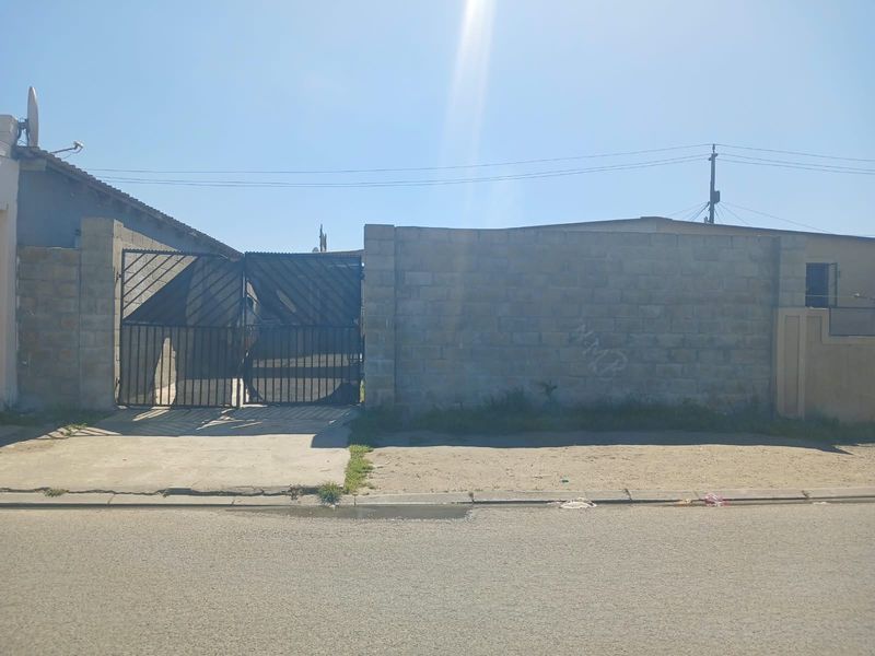 Front exterior view of the property featuring a concrete block boundary wall, metal driveway gate, and concrete driveway access from the street.