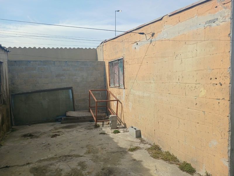 A rear exterior area featuring concrete block walls and a concrete slab floor, showing significant signs of weathering and deterioration.