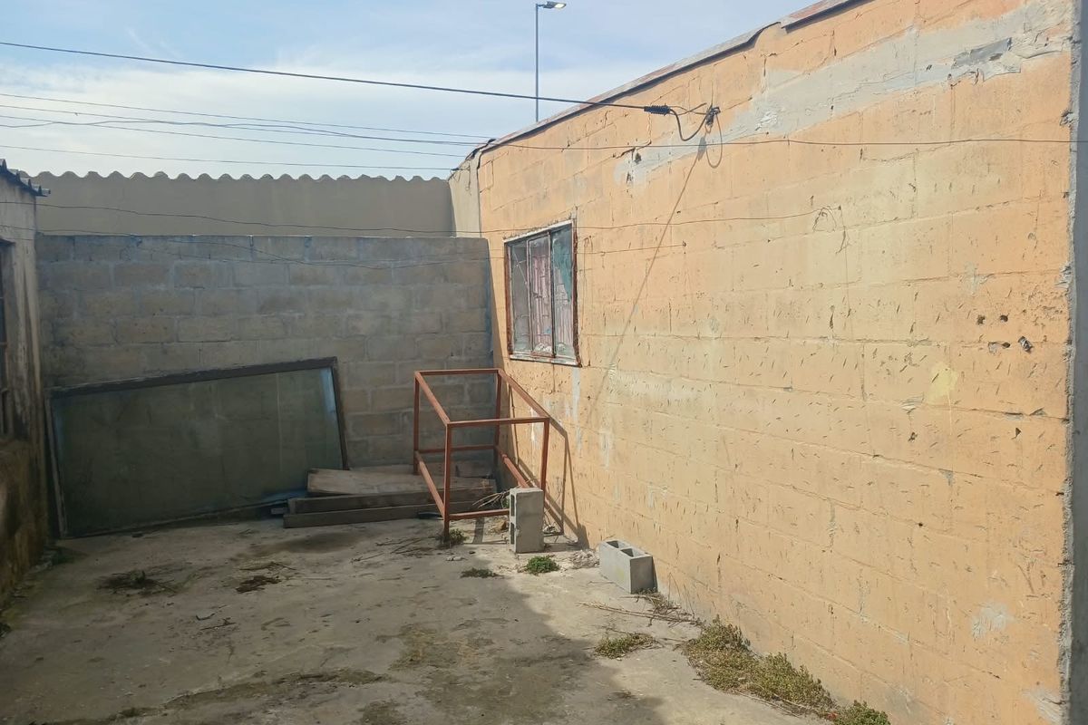 A rear exterior area featuring concrete block walls and a concrete slab floor, showing significant signs of weathering and deterioration.