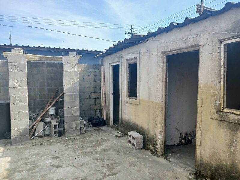 Rear exterior view of a property showing unfinished concrete block structures and weathered exterior walls requiring significant maintenance and repair.