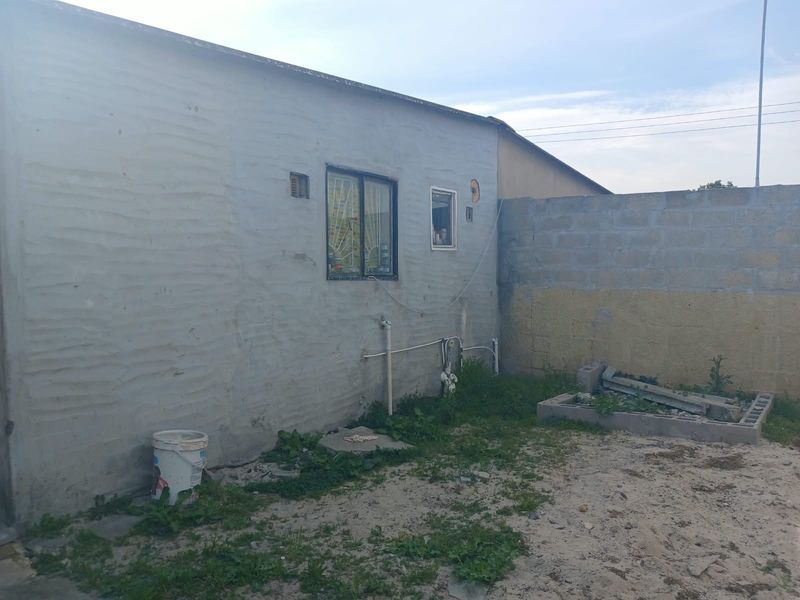 Rear exterior view of the property showing an unfinished plastered wall, exposed plumbing, and a concrete block boundary wall in a yard area.