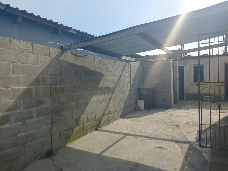 Rear courtyard area featuring concrete block boundary walls, paved flooring, and a basic metal roof structure.