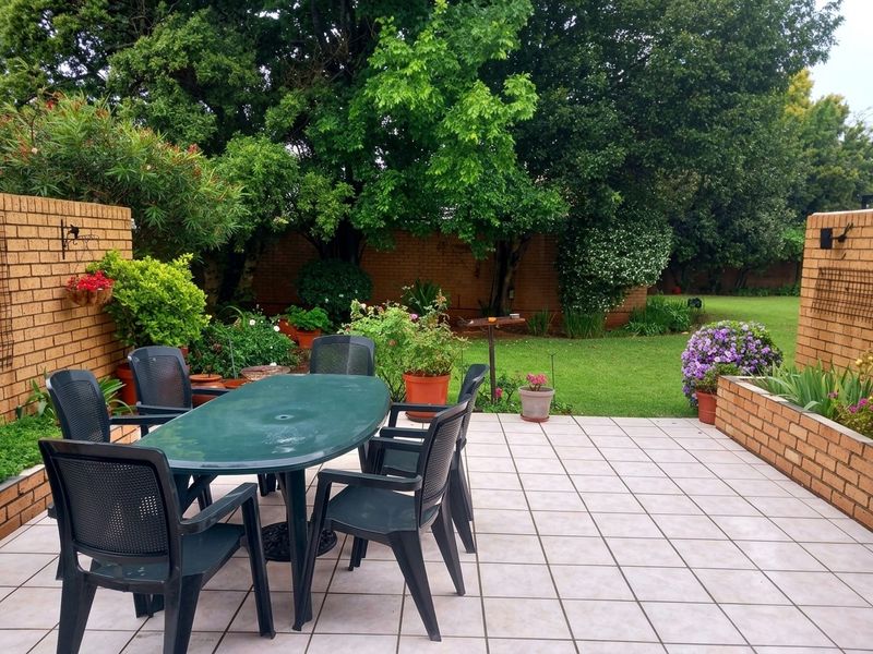 A spacious outdoor patio area featuring tiled flooring and brick retaining walls, overlooking a lush, well-maintained garden.