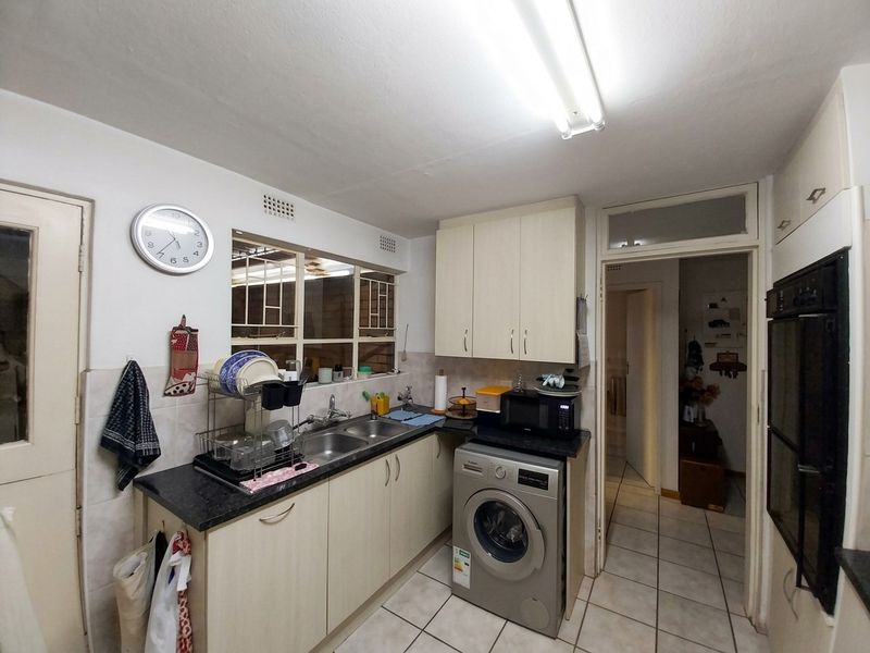 Functional kitchen featuring laminate cabinetry, double bowl sink, built-in oven, and tiled flooring with direct access to the hallway.