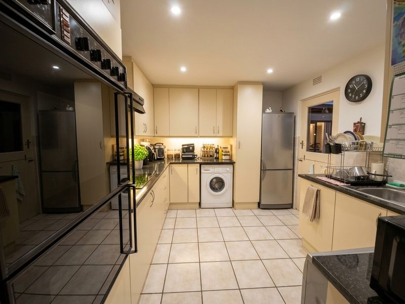 Functional kitchen featuring built-in cabinetry, double wall oven, ceramic hob, integrated washing machine, and tiled flooring with ample counter space.