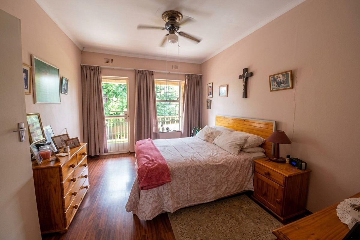 A well-lit bedroom featuring laminate flooring, a ceiling fan, and direct access to a private balcony through a sliding glass door.