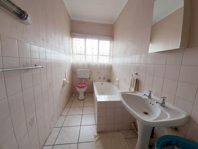 A dated bathroom featuring a pedestal basin, built-in bathtub, and toilet with neutral wall and floor tiling.