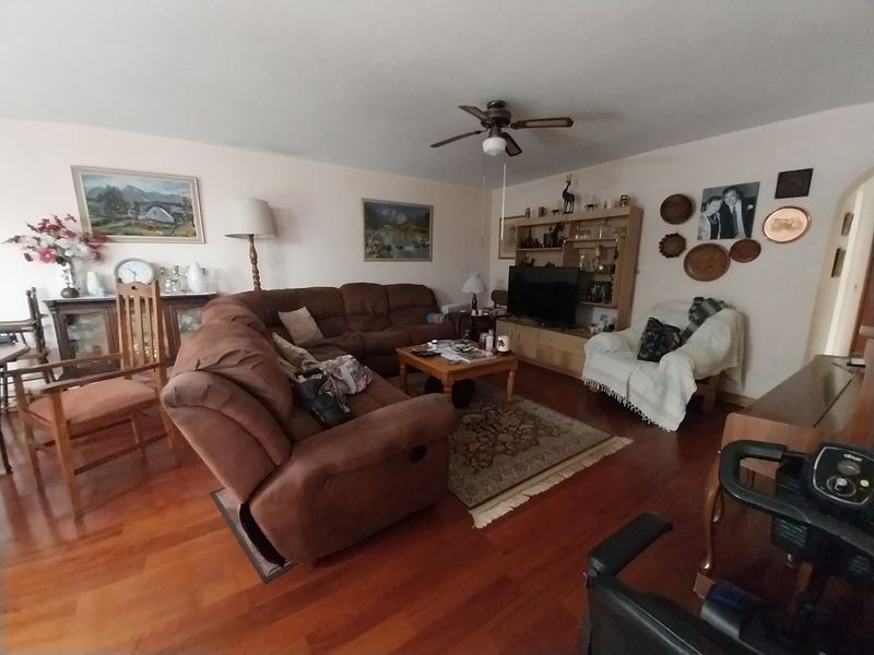 A spacious living room featuring warm hardwood flooring, a central ceiling fan, and a built-in shelving unit for storage and display.