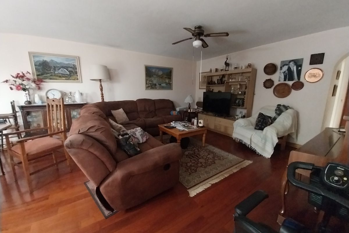 A spacious living room featuring warm hardwood flooring, a central ceiling fan, and a built-in shelving unit for storage and display.