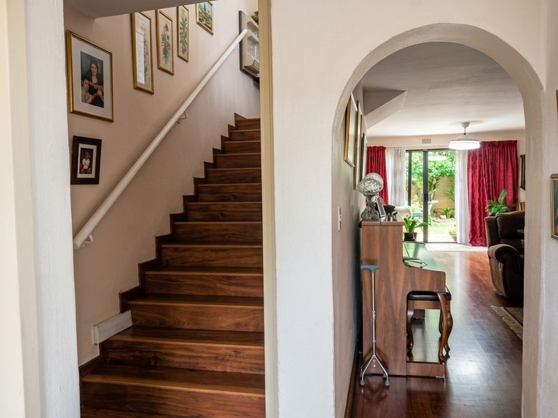 A welcoming hallway featuring a wooden staircase with a handrail, leading through an arched doorway into a bright living area with garden access.
